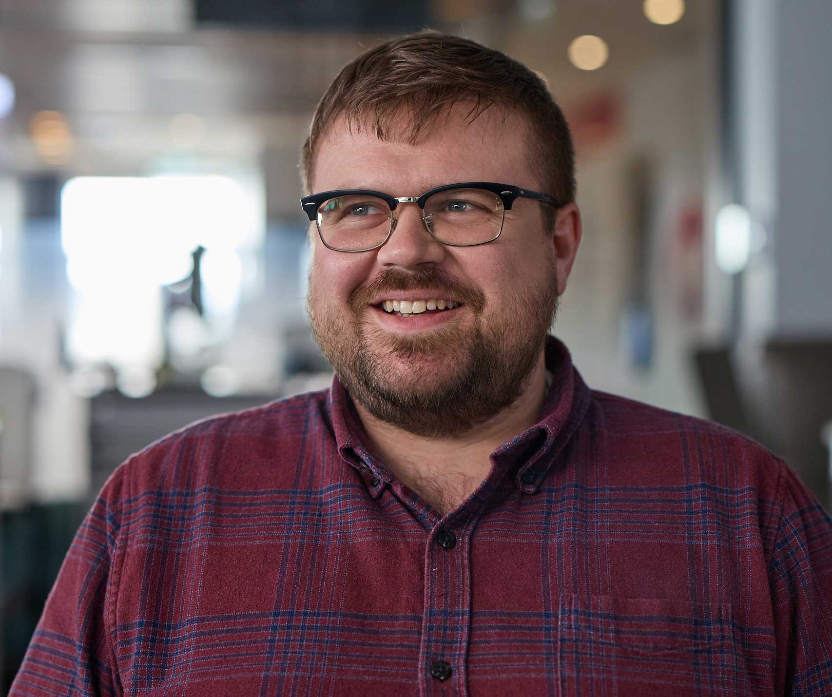 Ben, a blood donor, wearing a plaid shirt and glasses, looking just off to the side and smiling.