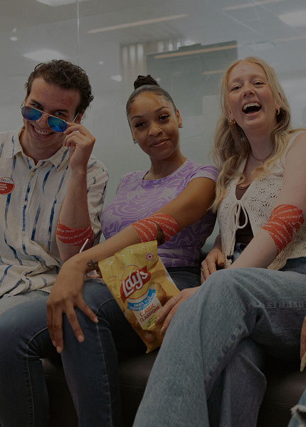 A group of young donors sitting together on a couch, laughing and sharing snacks while showing off their post-donation arm bandages.