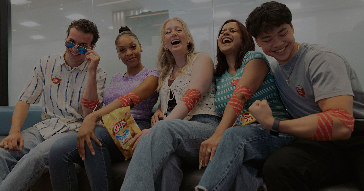 A group of young donors sitting together on a couch, laughing and sharing snacks while showing off their post-donation arm bandages.