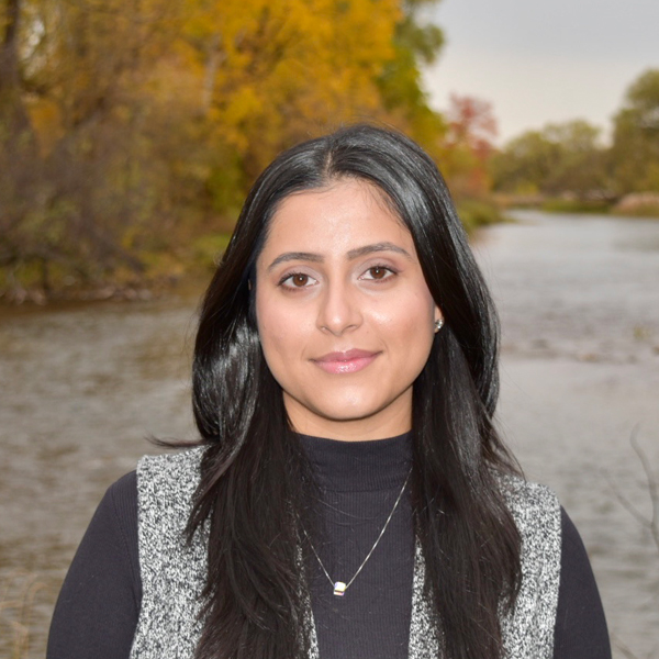 Image of peer recruiter Parmeet Kahlon standing in front of a lake with trees in the back.