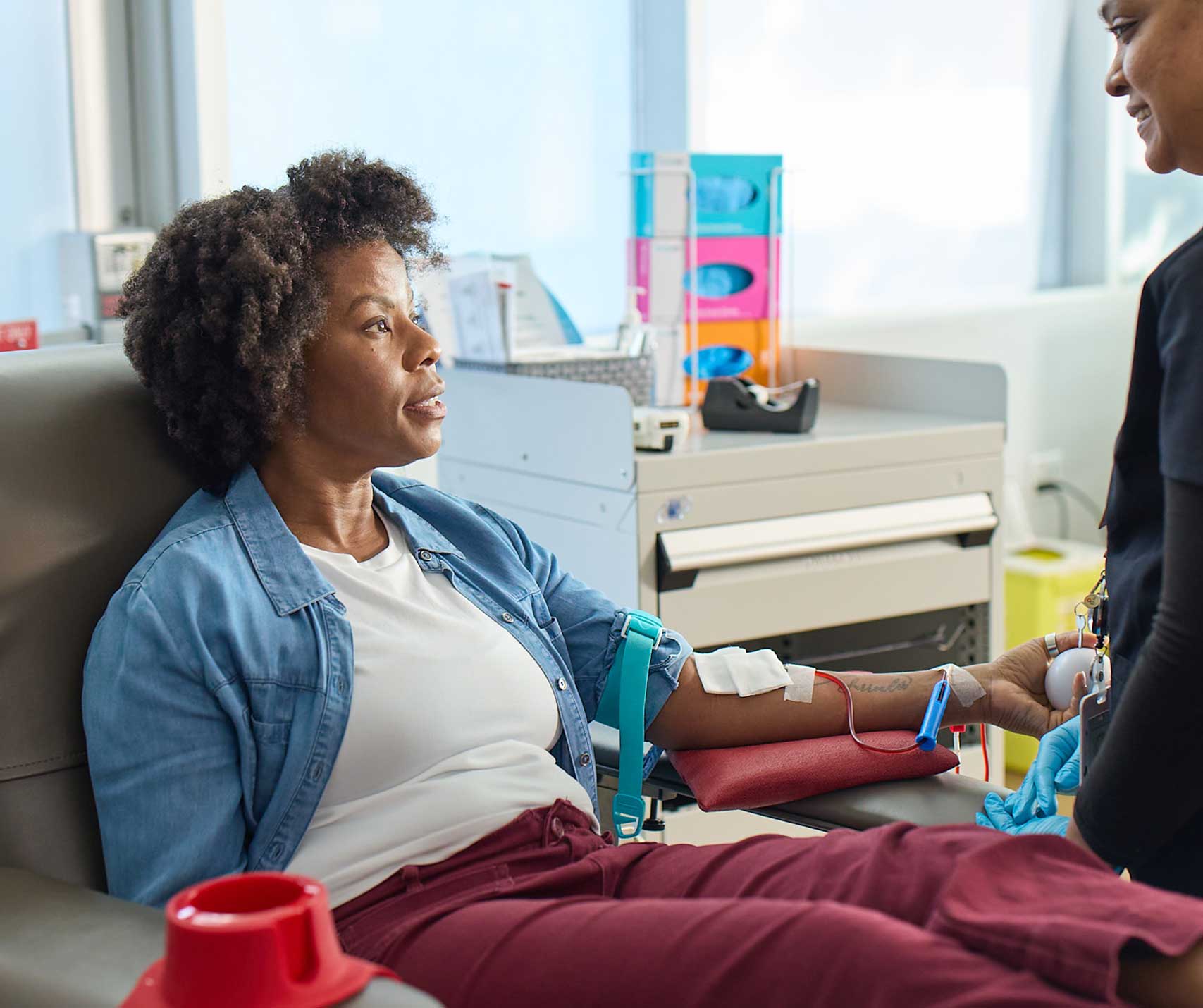 Julie, a blood donor, sitting in a donation chair while donating blood, looking up at the nurse who is taking care of her.