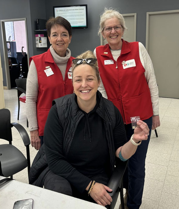 Two women in red vests standing behind a woman sitting in a chair