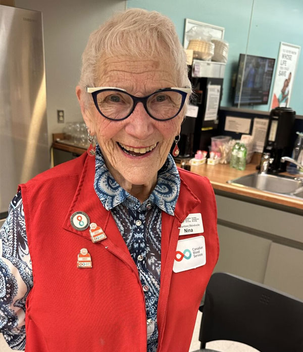 woman in red vest standing in kitchen with arms crossed behind her back