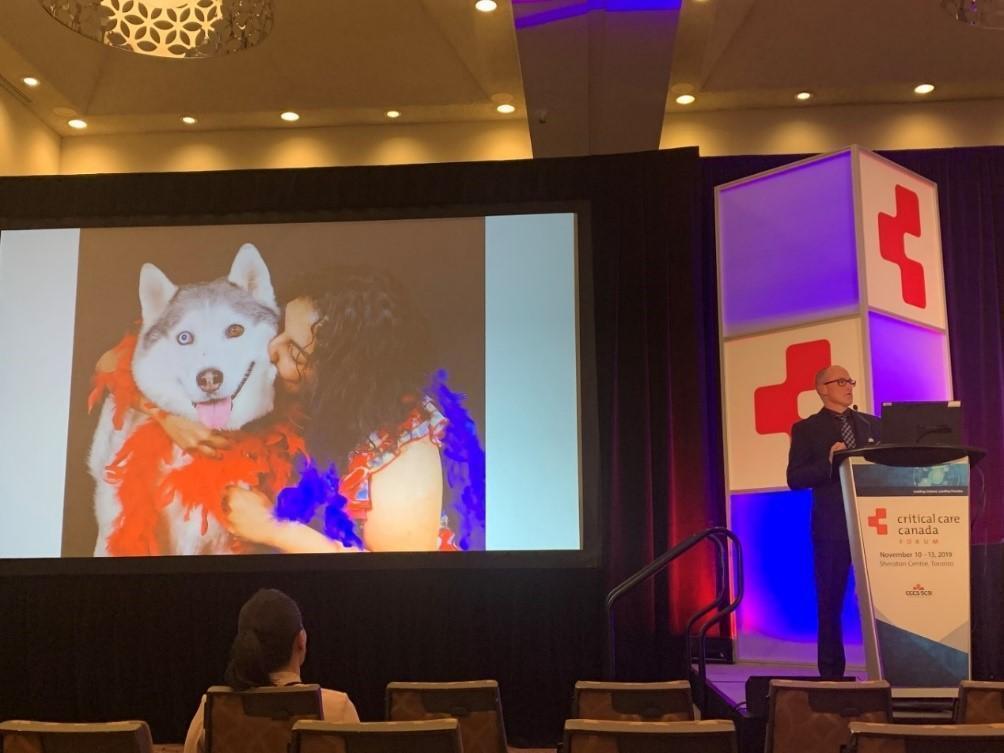 Randall Tressider presents at Canadian Critical Care Forum in 2019, alongside a photo of his deceased wife Shelly Sarwal