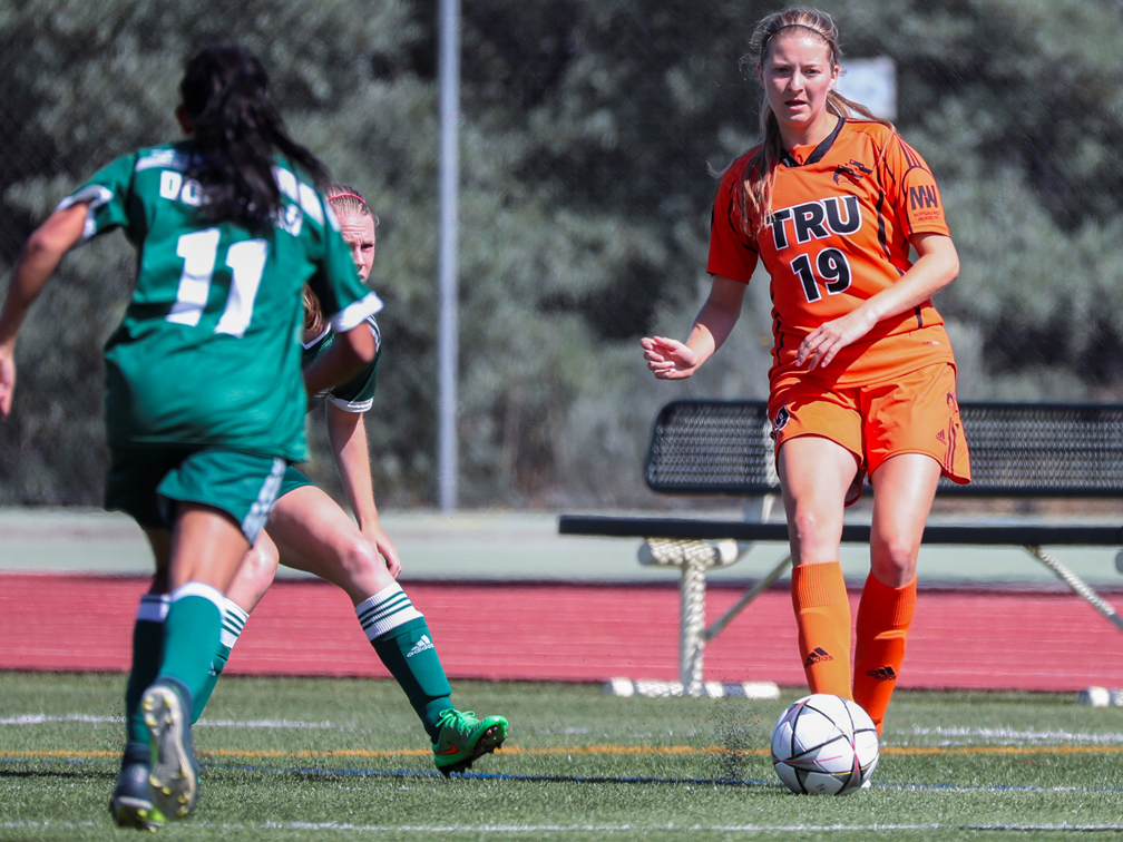 Woman in team uniform passes a soccer ball forward