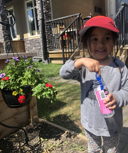 Petite fille debout dans la cour avec une baguette à bulles et un flacon de liquide à bulles.