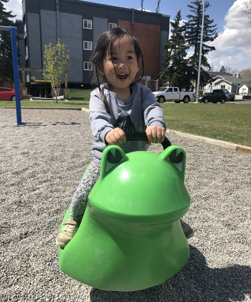 Petite fille assise sur un siège de jeu en forme de grenouille dans une aire de jeux.