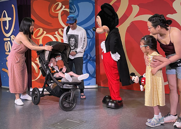 Enfant dans une poussette faisant signe à Mickey Mouse, sous le regard des membres de sa famille.