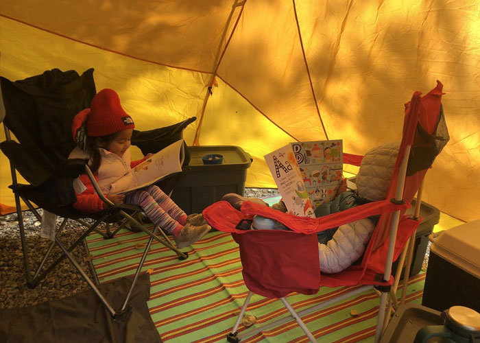 Receveuse de sang et sa sœur dans des chaises de camping à l’intérieur d’une tente, en train de lire des livres.
