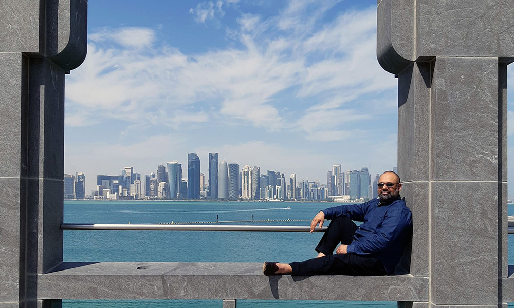 Un homme assis sur une structure, avec la silhouette de Doha en toile de fond