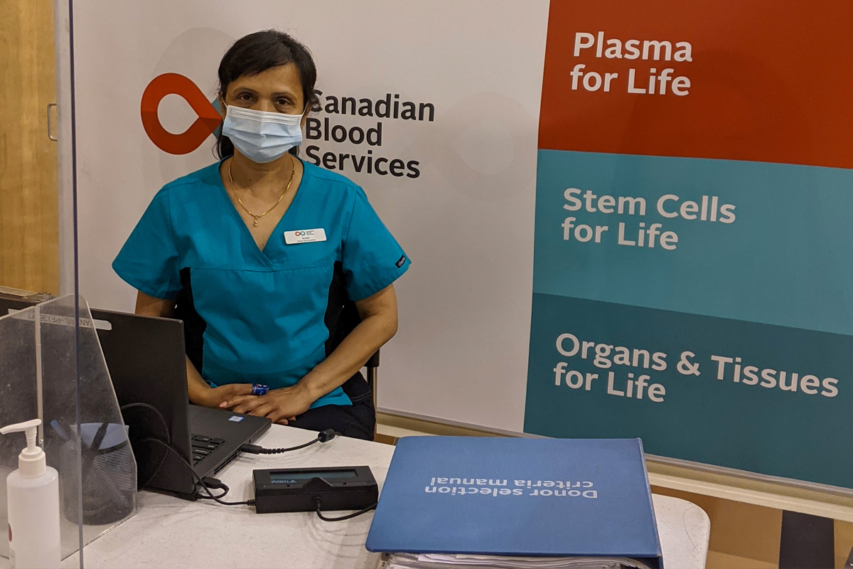 Canadian Blood Services donor care associate in Vancouver poses in a donor centre with the branding sign behind her.