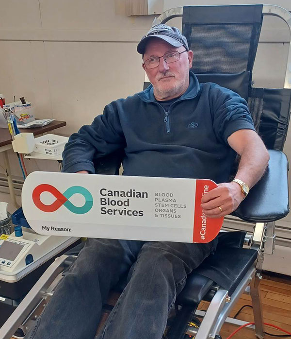 Blood donor in donation chair holding Canadian Blood Services sign