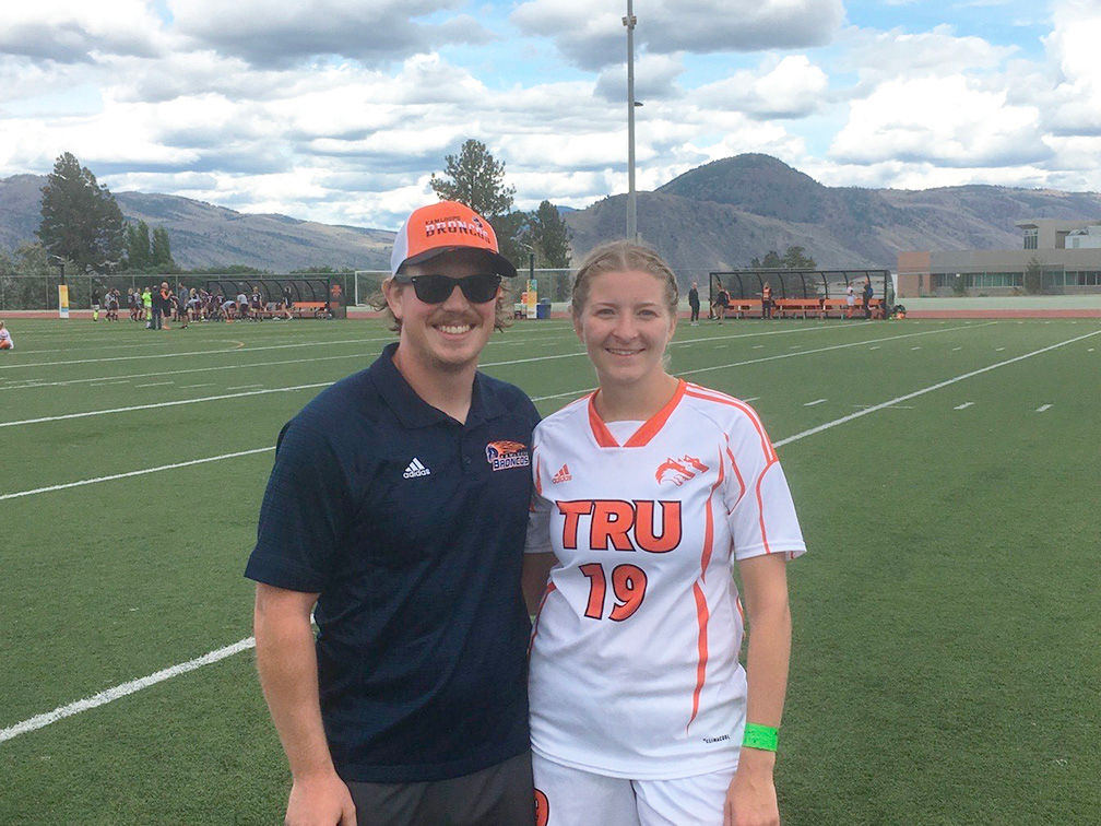 Kamloops Broncos Football Club head coach Braden Vankoughnett stands on a field beside his girlfriend Kelsey Thorkelsson, who has aplastic anemia and needs regular blood transfusions.
