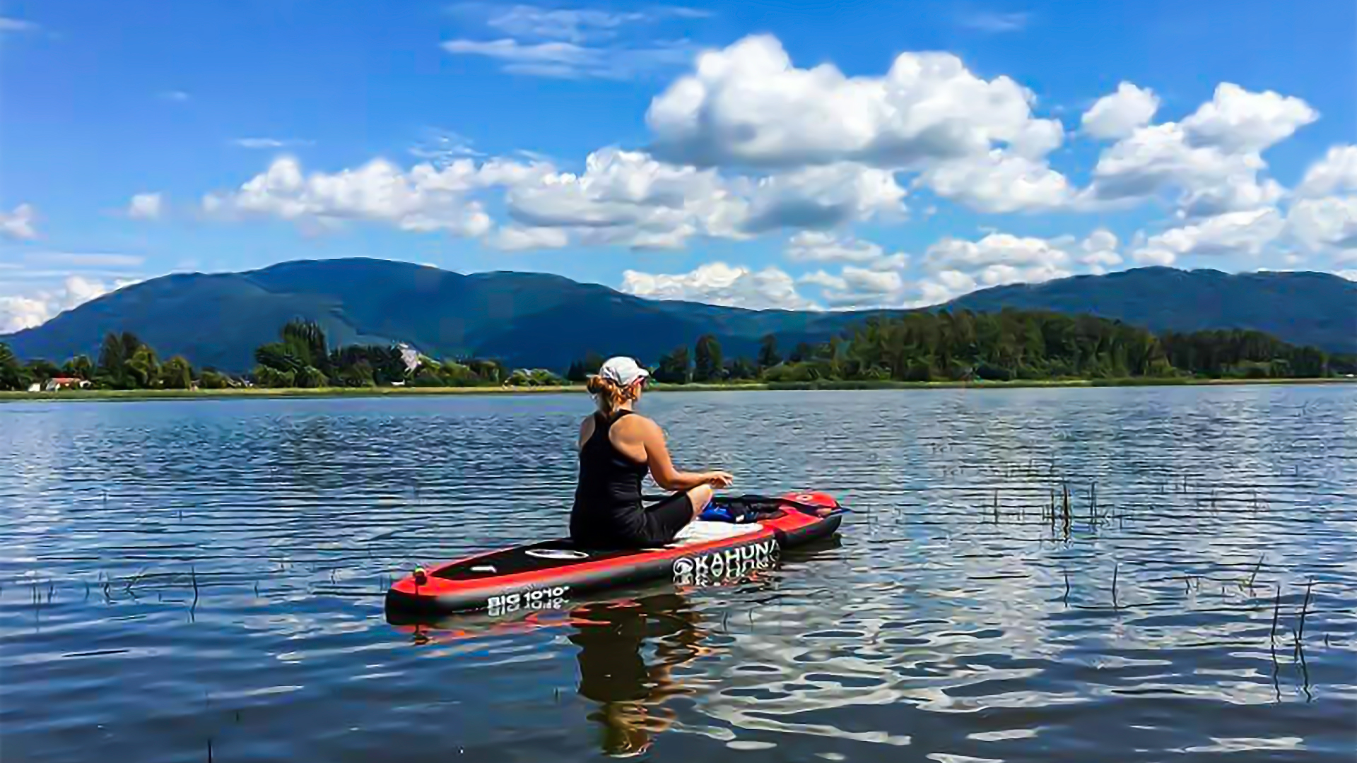Image of lifesaving kidney recipient Linda Paul in sitting yoga pose on a paddle board on the water