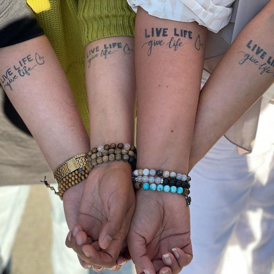 Group of hands together showing matching tattoos that say "live life give life"