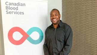 Image of Dujon Donaldson standing beside a Canadian Blood Services banner stand