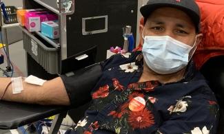 A man with a black floral shirt sitting in a chair donating blood wearing a face mask at the donor centre in Calgary.