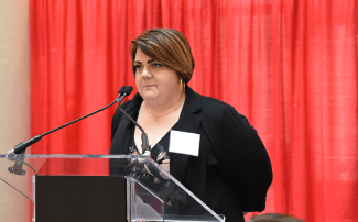 Becky Littau standing in behind a podium speaking at the Corporate Luncheon
