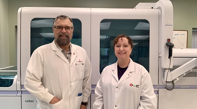 Douglas Ems &amp; Valerie Conrod in front of a large machine wearing white lab coats