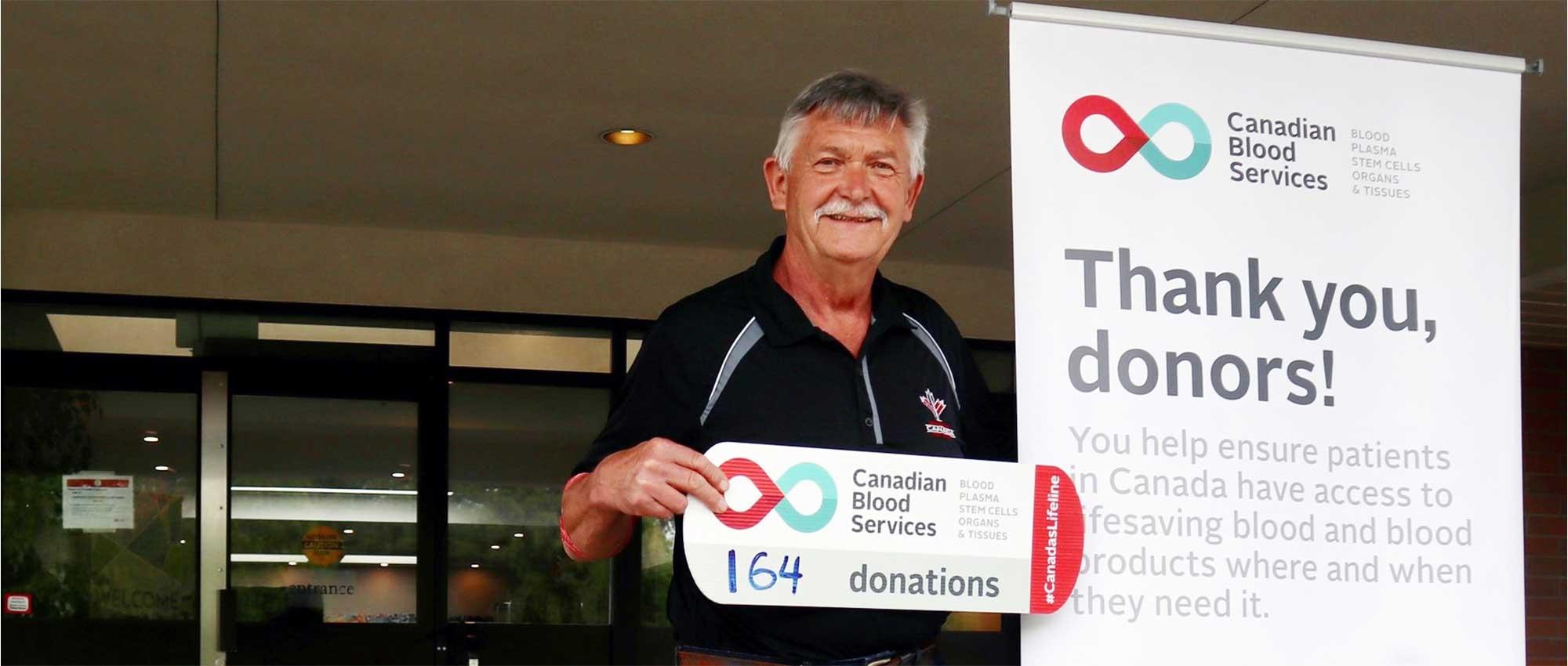 Blood donor stands next to a sign that says Thank you, donors