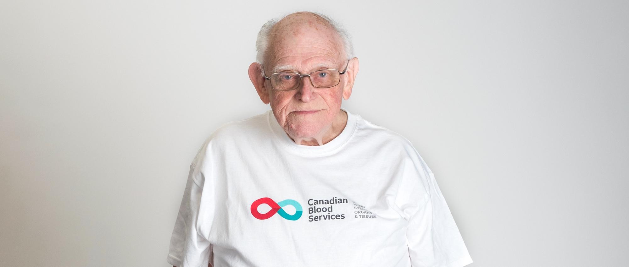 Thumbnail image of Bob Kerr wearing a Canadian Blood Services T-shirt standing in front of a white wall.