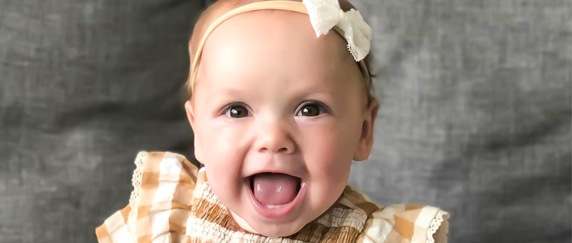 Image of baby blood recipient Madison Lewis sitting in front of a grey backdrop smiling.
