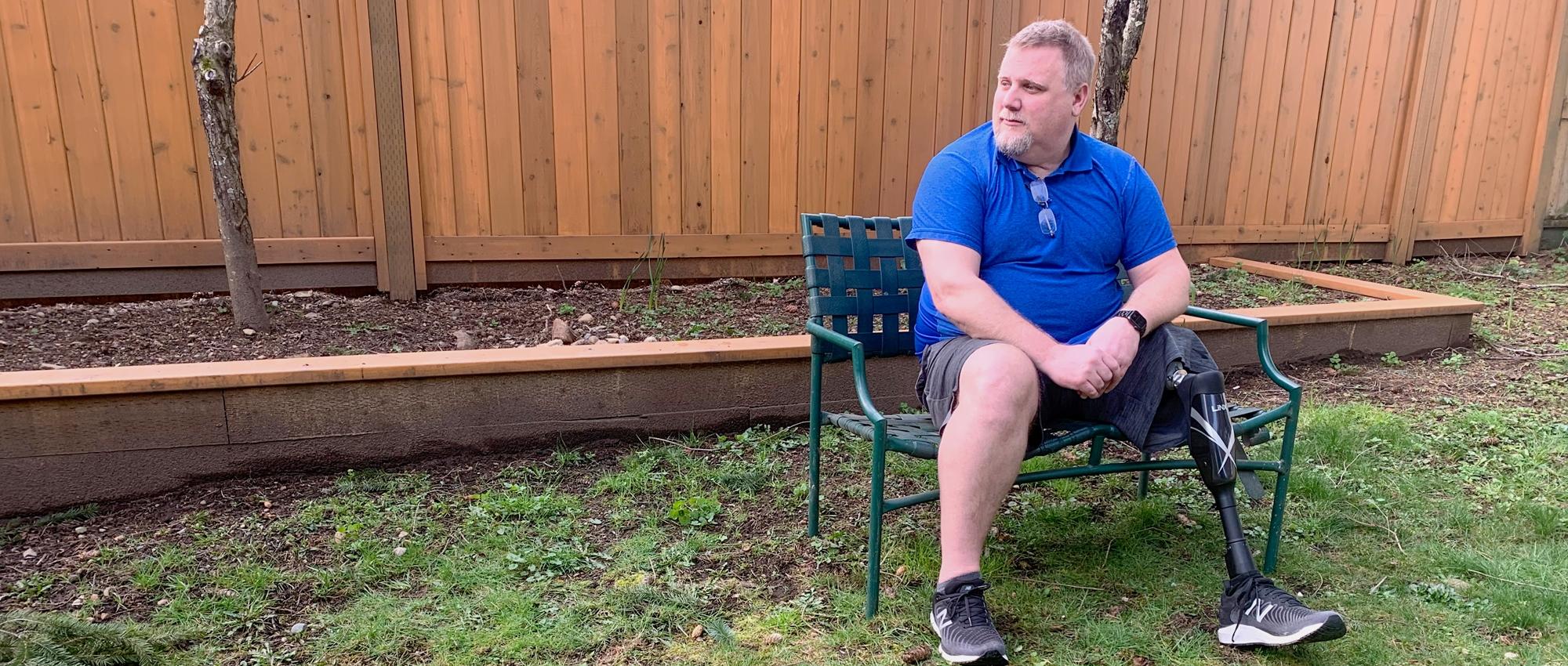 A man with a prosthetic leg sits on a bench outdoors.