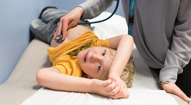Boy in yellow shirt on hospital bed being checked with a stethoscope